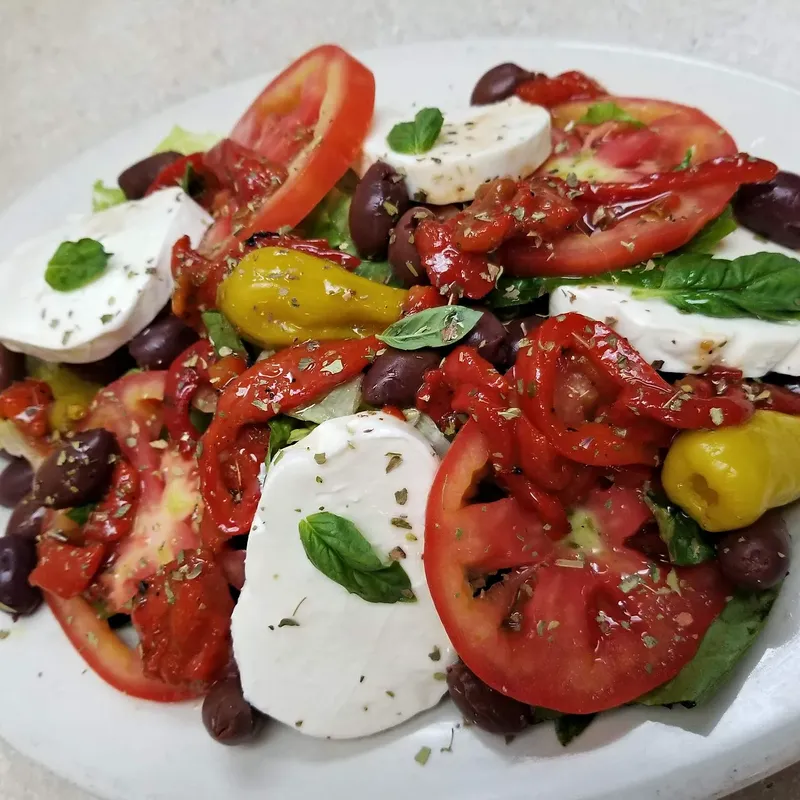 A caprese salad with fresh mozzarella, tomato, roasted peppers and olives