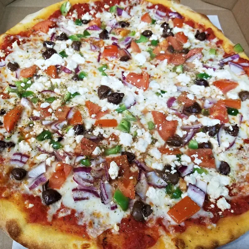 A Greek-style pizza with feta, olives, red onion, tomato and peppers in the box