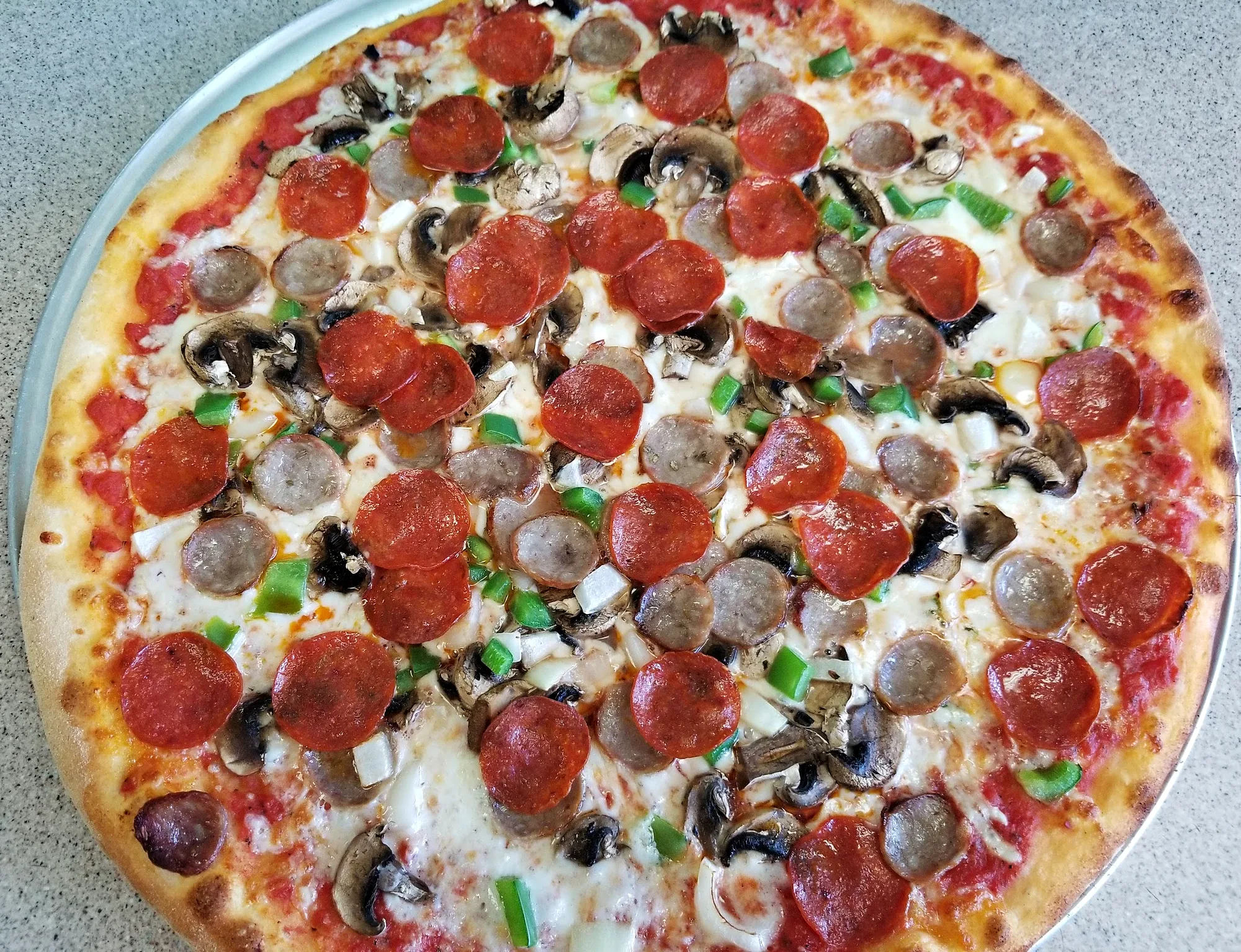 A round pizza loaded with pepperoni, sausage, mushrooms and green peppers